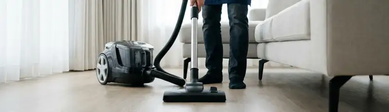 Professional house cleaner vacuuming a living room floor with a canister vacuum cleaner, Charlotte, NC.