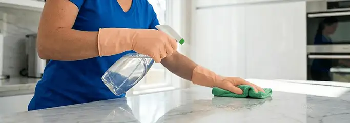 Maid service worker spraying and wiping a kitchen countertop with a microfiber cloth for sanitizing, Charlotte, NC.