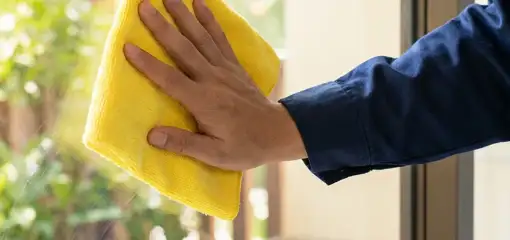 House cleaner wiping a glass window with a yellow microfiber cloth for streak-free cleaning, Charlotte, NC.